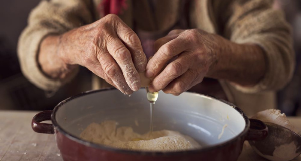 Senior woman’s hands cracking an egg into a mixing bowl.