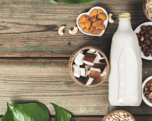 Dairy free glass bottle of milk with various ingredients that dairy-free milk can be made from in various bowls surrounding the milk.