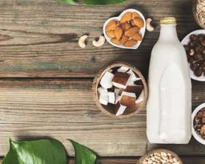 Dairy free glass bottle of milk with various ingredients that dairy-free milk can be made from in various bowls surrounding the milk.