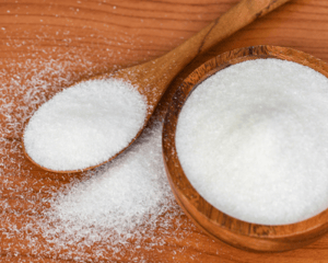 Table salt in a wooden bowl and wooden spoon on a wood table.