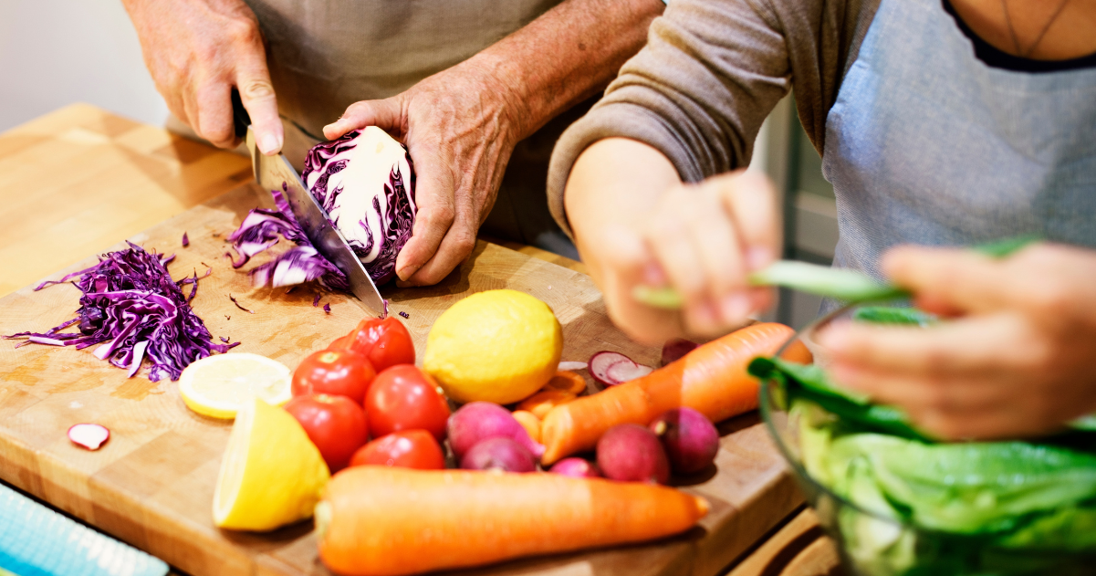 Seniors couples’ hands preparing Mediterranean vegetables on wooden cutting boards in their kitchen at home.