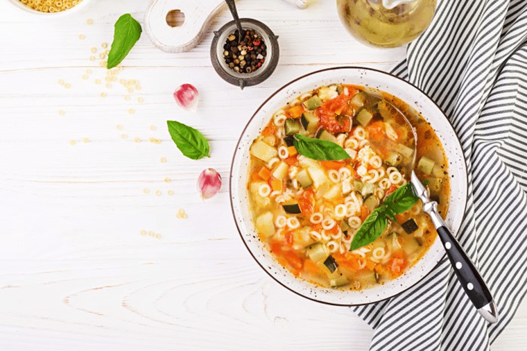 Bowl of minestrone soup with pasta and vegetables on white table