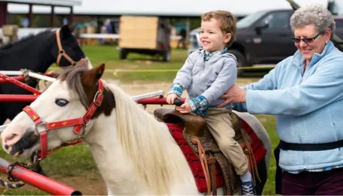 child riding a pony with their granparent