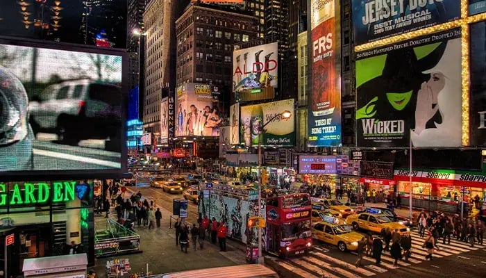 Bustling Times Square at night with bright billboards, yellow taxis, and crowds of people walking through the streets