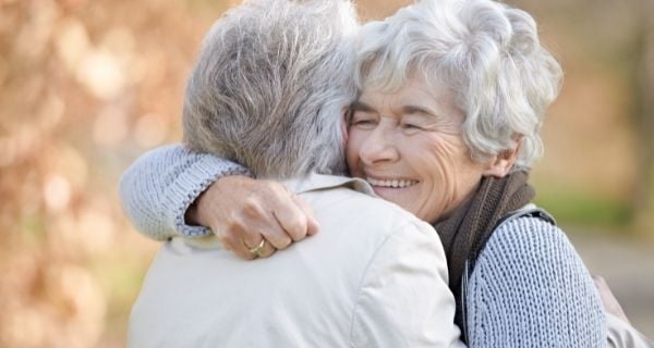 Two senior women showing kindness to one another with a hug.