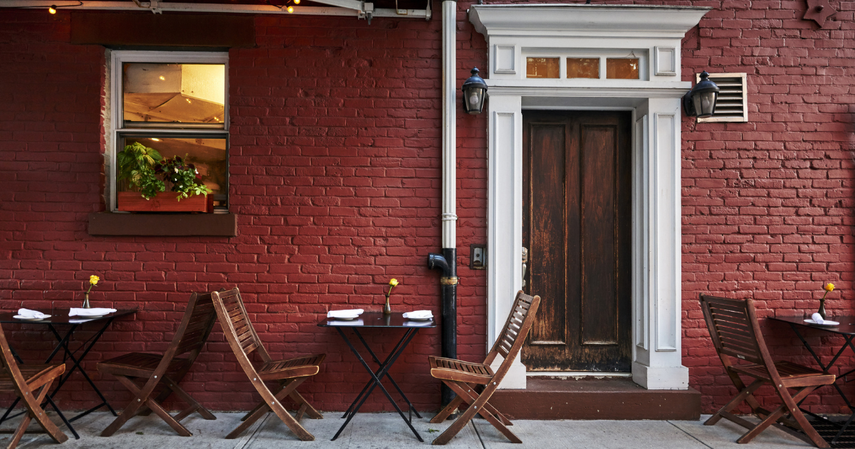 Outdoor seating against a red painted brick wall at an Upper West Side restaurant.