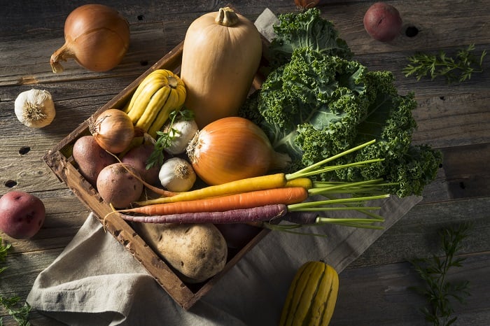 Onions, squash, carrots, and kale in a wooden crate