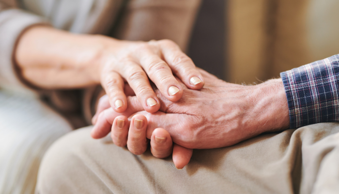 Caregiver holding hand of loved one with Alzheimer's disease to help with aggression and agitation associated with dementia.