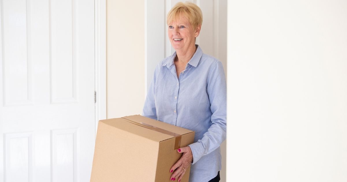 Older woman walking into a room while carrying a box