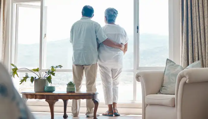 Mature couple with their arms around each other looking out a balcony window to the ocean