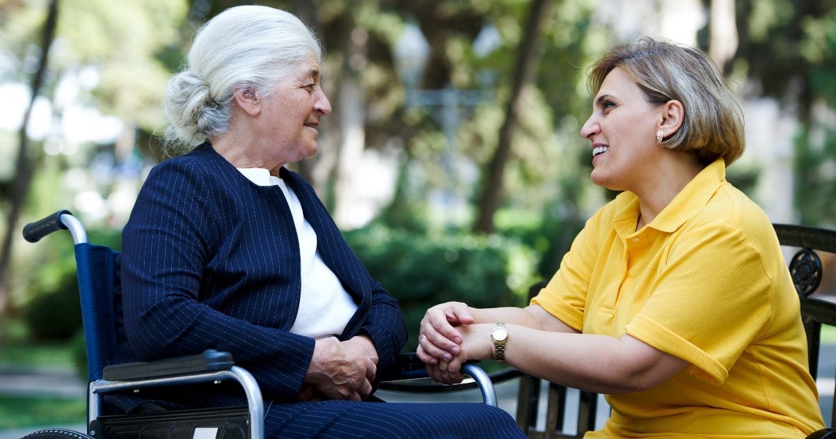 Woman sitting and smiling with a mature lady with alzheimers.