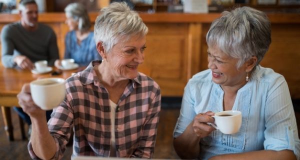 Two senior women at a coffee shop together talking and catching up.