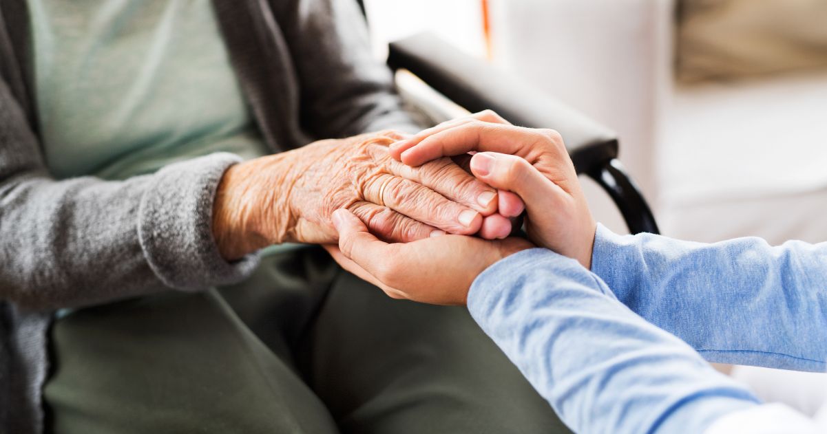 Caregiver holding the hands of a person in a wheelchair with Alzheimer’s disease.