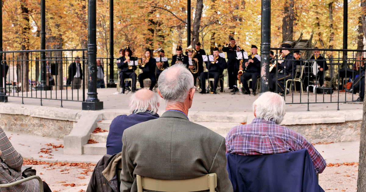 Seniors in a park listening to an orchestra.