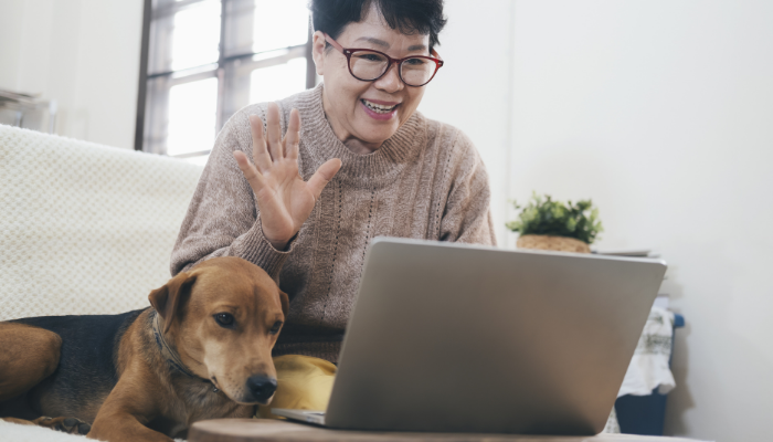 Woman with dog by her side has a virtual call with her loved one using her laptop