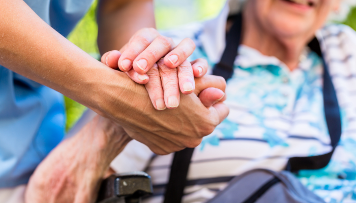 Caregiver holding the hand of a mature adult. 